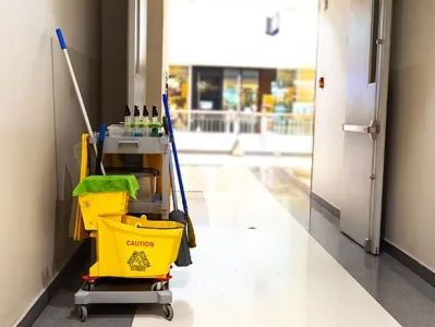 Chariot de nettoyage équipé de seaux, serpillière et produits d’entretien dans un couloir intérieur.